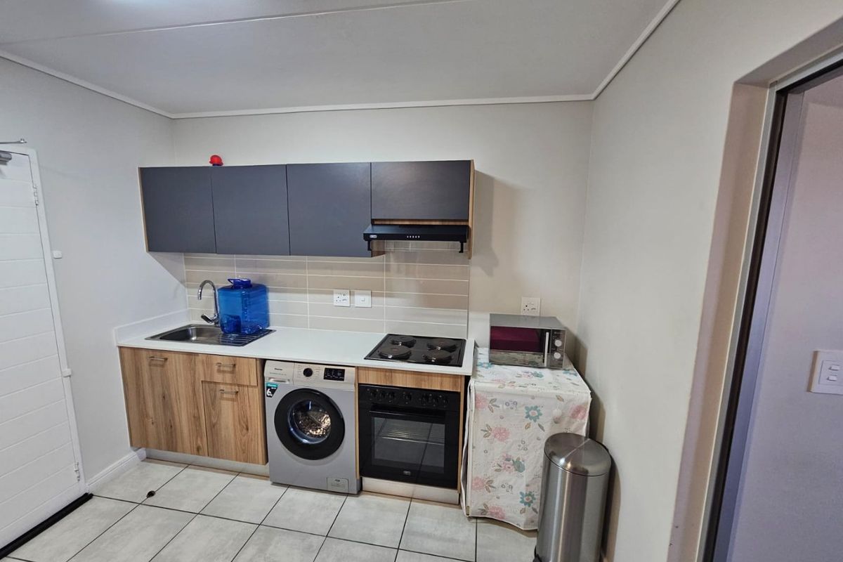 Compact kitchen featuring modern wood-grain and dark grey cabinetry, integrated oven and hob, tiled backsplash, and tiled flooring.