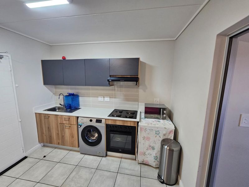 Compact kitchen featuring modern wood-grain and dark grey cabinetry, integrated oven and hob, tiled backsplash, and tiled flooring.
