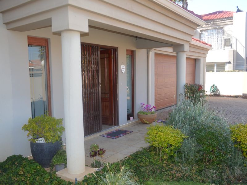 Front entrance of the townhouse featuring a covered porch with concrete columns, a security gate, and an integrated double garage with paved driveway access.