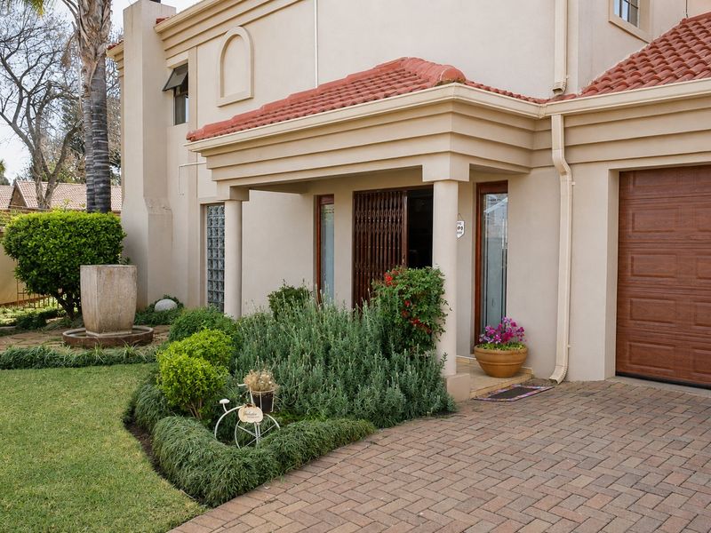 Front elevation of a townhouse featuring a paved driveway, single garage, covered entrance porch, and a landscaped garden with a stone water feature.