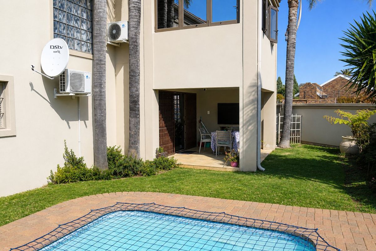 Rear exterior view featuring a swimming pool with safety net, brick paved surround, and a covered patio area attached to the townhouse structure.