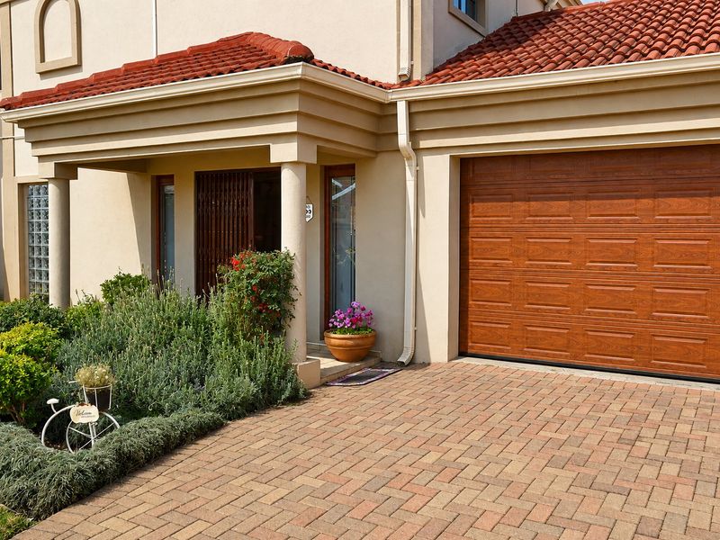 Front elevation of a townhouse featuring a paved driveway, a wood-look sectional garage door, and a covered entrance with decorative columns.