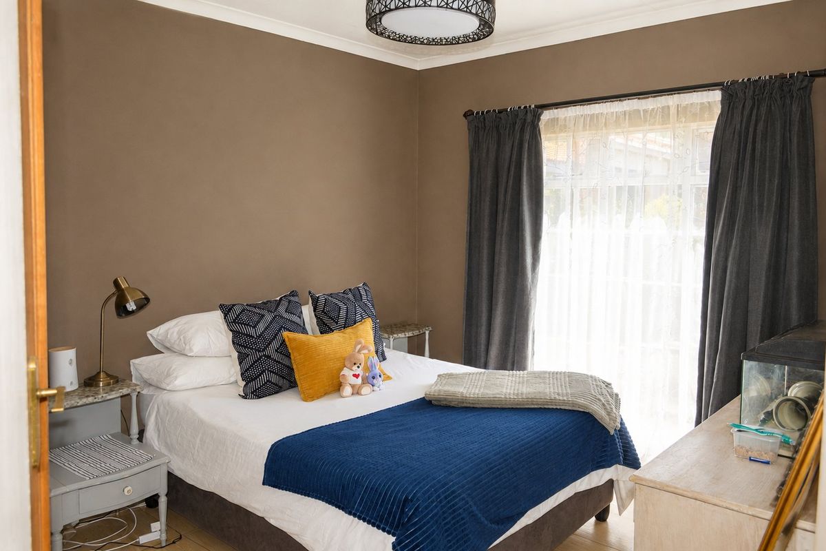 A cozy bedroom featuring neutral wall tones, a large window with curtain rod, and a central ceiling light fixture.