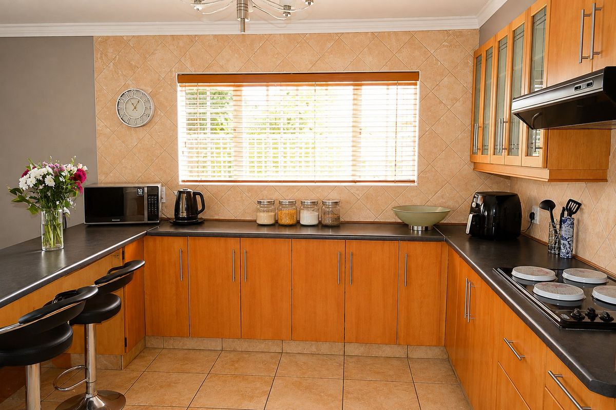 A functional kitchen featuring wooden cabinetry, dark laminate countertops, a built-in hob with extractor fan, and tiled backsplash and flooring.