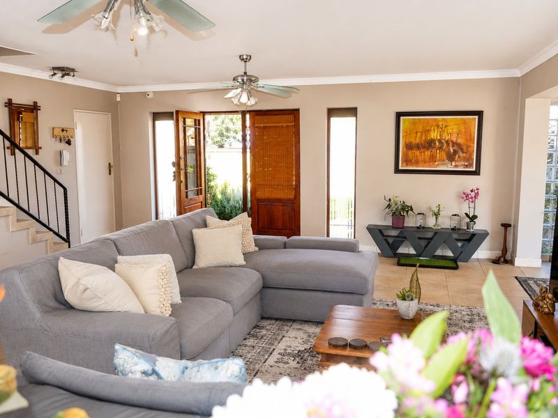 Spacious living room featuring tiled flooring, ceiling fans, a staircase with metal balustrade, and a feature glass block wall near the entrance.