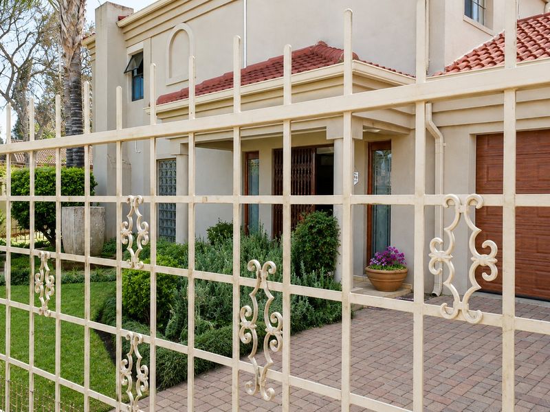 Front view of a townhouse featuring a paved driveway, sectional garage door, and secure wrought iron fencing.