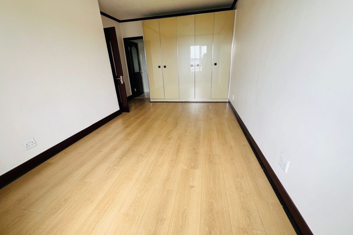 A clean, empty bedroom featuring light wood-look laminate flooring and modern high-gloss built-in cupboards with dark trim accents.