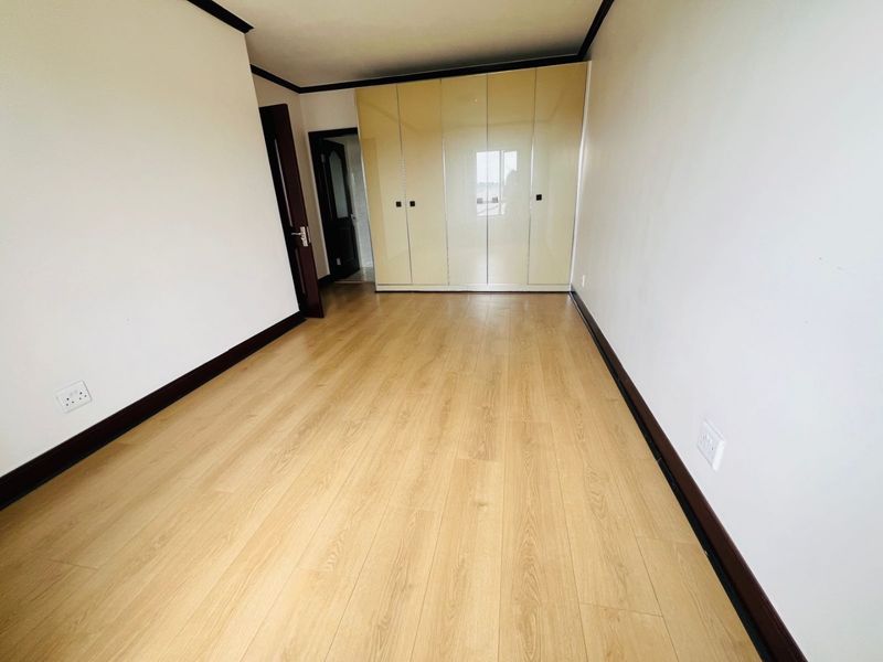 A clean, empty bedroom featuring light wood-look laminate flooring and modern high-gloss built-in cupboards with dark trim accents.