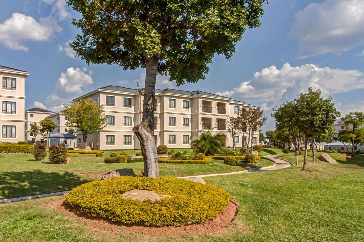 A view of the apartment complex exterior featuring well-maintained landscaped gardens, mature trees, and paved walkways between the residential buildings.