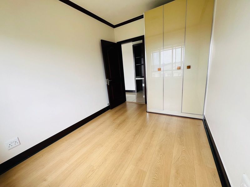 A bright, empty bedroom featuring light wood-look laminate flooring, a built-in wardrobe with glossy finish, and dark contrasting trim.