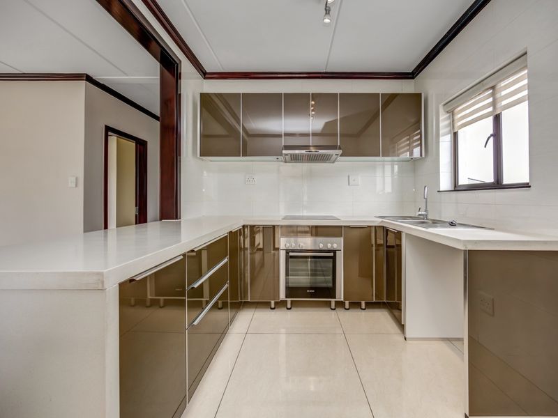 Modern kitchen featuring high-gloss cabinetry, stone countertops, integrated oven and hob, and tiled finishes in a clean, functional layout.