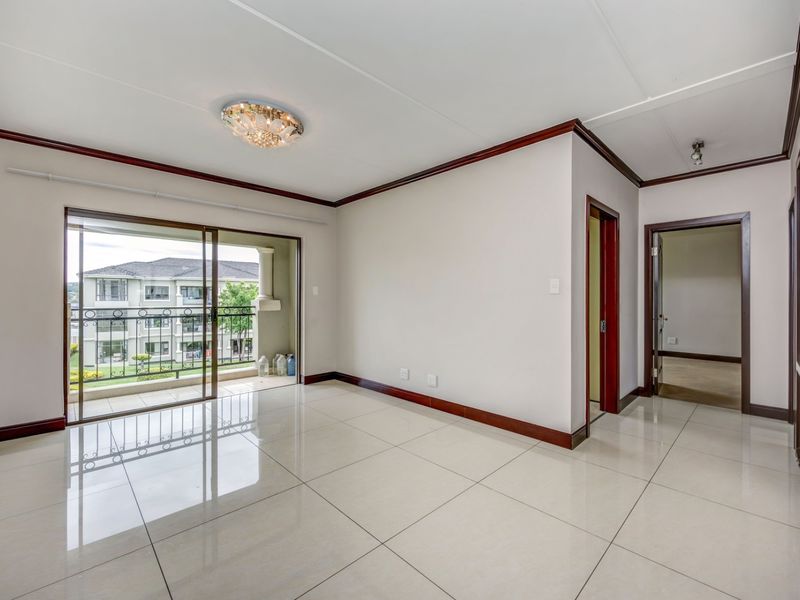A bright, empty living room featuring polished tile floors, dark wood trim, and a sliding glass door leading to a private balcony.
