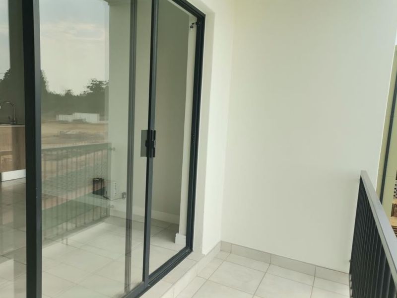 A clean, modern balcony featuring tiled flooring, a black metal balustrade, and large sliding glass doors leading into the apartment interior.