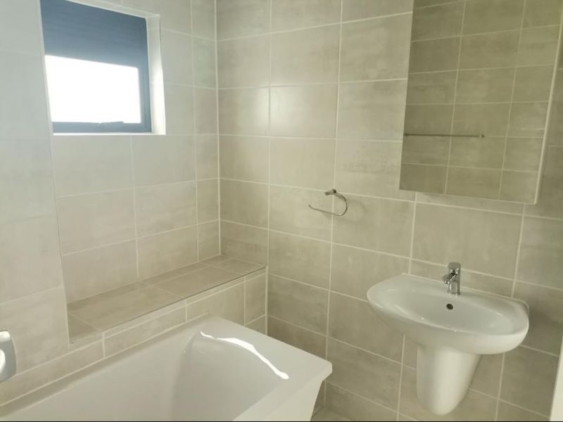 A clean, modern bathroom featuring a pedestal basin, built-in bathtub, and neutral wall tiling with a functional layout.