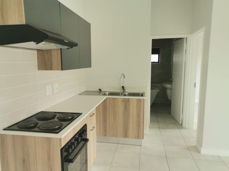 Modern kitchen featuring wood-look cabinetry, built-in electric stove and oven, extractor fan, and tiled flooring, with an adjacent bathroom visible.