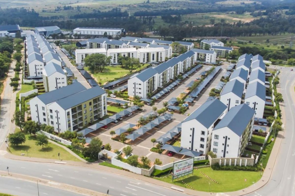 Aerial view of a modern residential apartment complex featuring multiple buildings, paved parking areas with carports, and landscaped communal grounds.