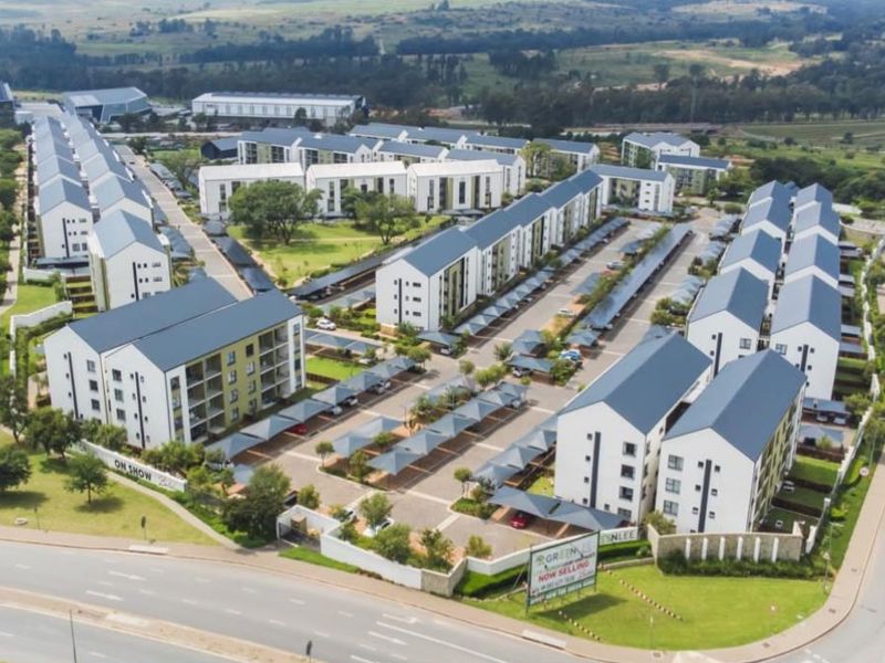 Aerial view of a modern residential apartment complex featuring multiple buildings, paved parking areas with carports, and landscaped communal grounds.