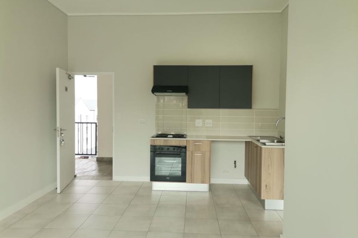 A clean, modern kitchen featuring light wood-finish cabinetry, a built-in oven with gas hob, tiled splashback, and direct access to an outdoor balcony area.