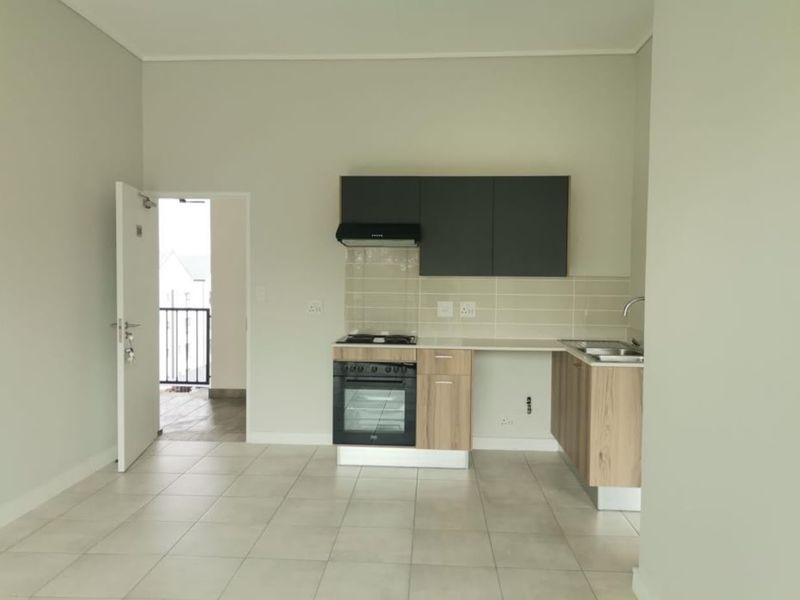 A clean, modern kitchen featuring light wood-finish cabinetry, a built-in oven with gas hob, tiled splashback, and direct access to an outdoor balcony area.