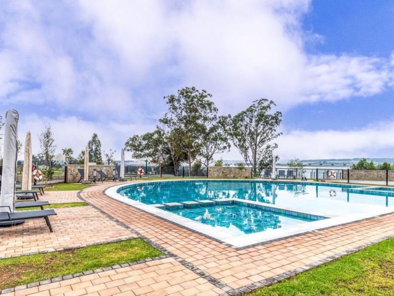A well-maintained outdoor swimming pool area featuring a paved deck, stone perimeter wall, and landscaped surroundings in a residential estate setting.