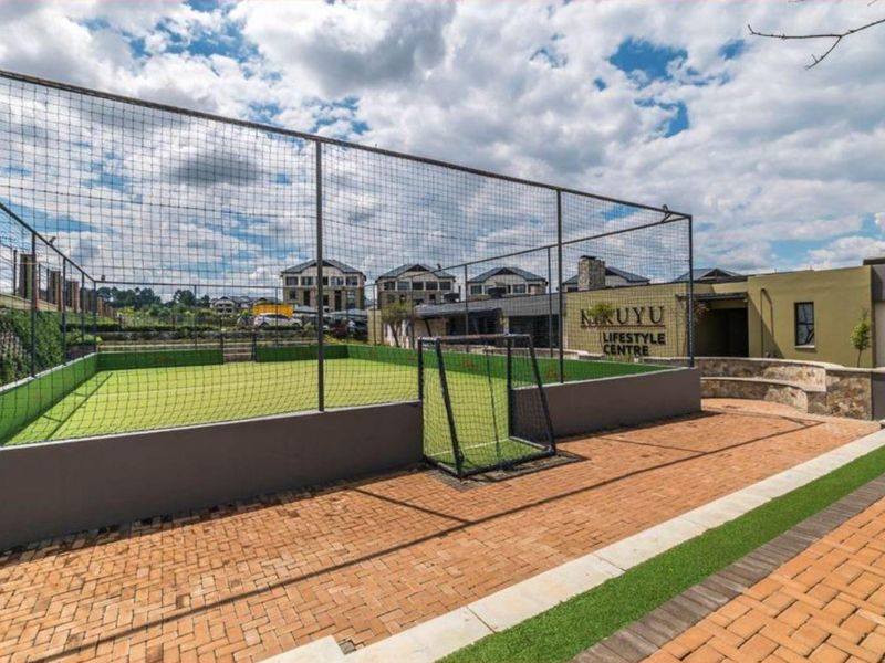 Outdoor sports facility featuring an enclosed artificial turf soccer court with perimeter fencing and adjacent paved walkways within the lifestyle centre.