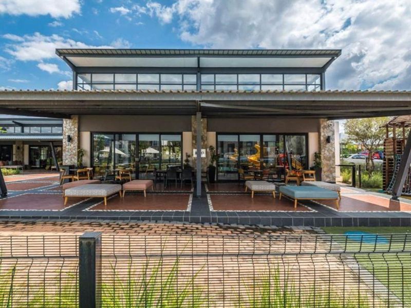 A spacious covered patio area featuring modern sliding glass doors, stone-clad pillars, and durable tiled flooring, ideal for outdoor relaxation and entertainment.