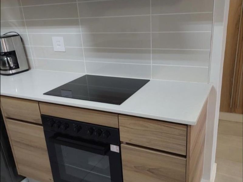 Modern kitchen featuring sleek laminate cabinetry, quartz countertops, a built-in oven with electric hob, and a contemporary tiled backsplash.