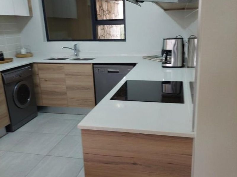Modern kitchen featuring wood-finish cabinetry, stone countertops, integrated appliances, and a sleek electric hob with an extractor fan.