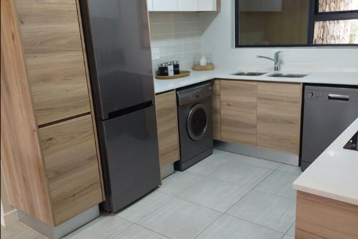 Modern kitchen featuring wood-grain cabinetry, white countertops, tiled flooring, and integrated appliance spaces with a large window for natural light.