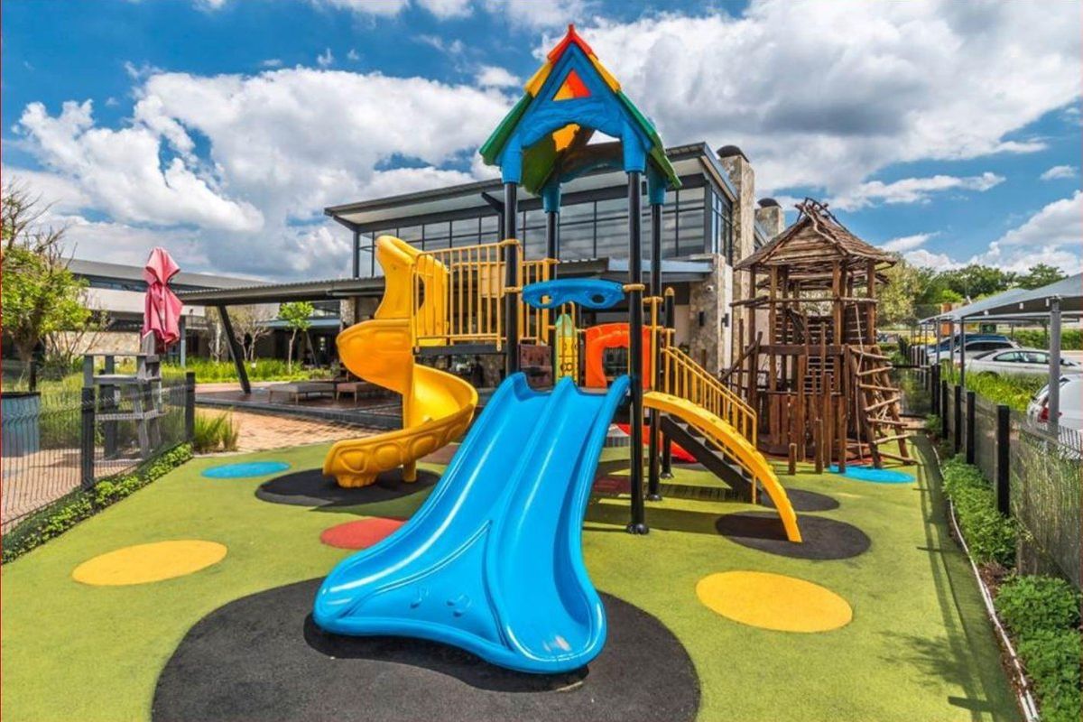 A well-maintained outdoor playground area featuring colorful play structures and safety flooring, situated in the rear communal space of the apartment complex.