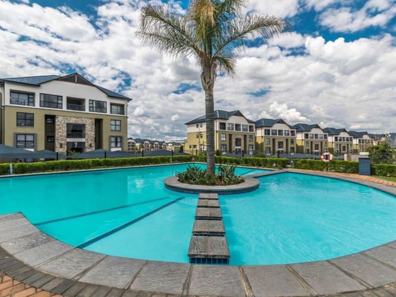 A well-maintained communal swimming pool area featuring stone coping, stepping stones, and landscaped hedging, set within a modern apartment complex.