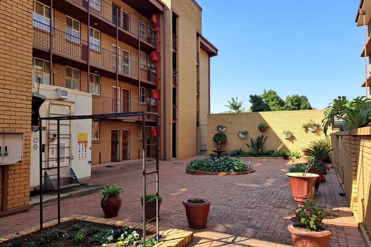 A paved rear courtyard area of an apartment complex featuring brick walls, raised garden beds, and metal fire escape access.