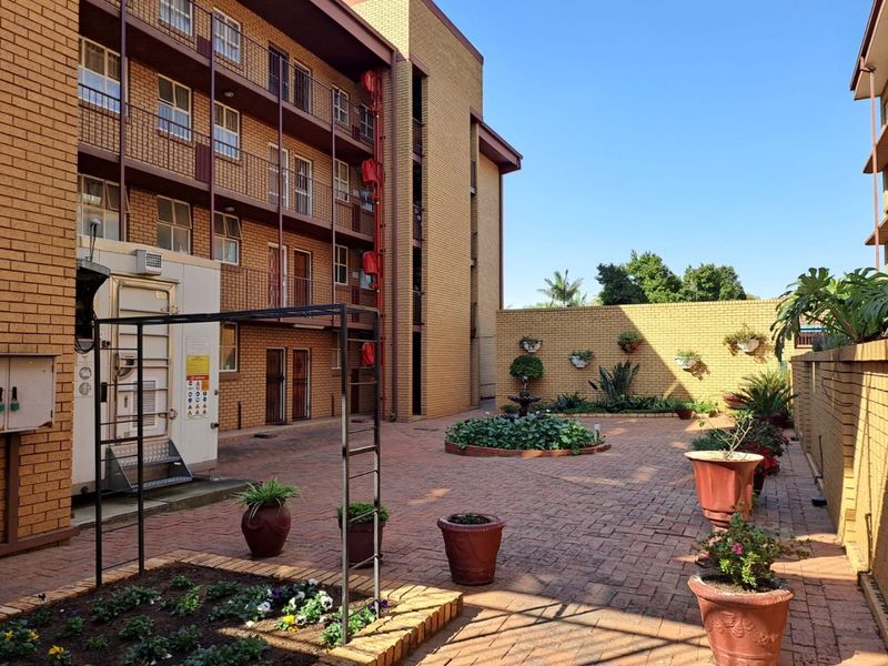 A paved rear courtyard area of an apartment complex featuring brick walls, raised garden beds, and metal fire escape access.