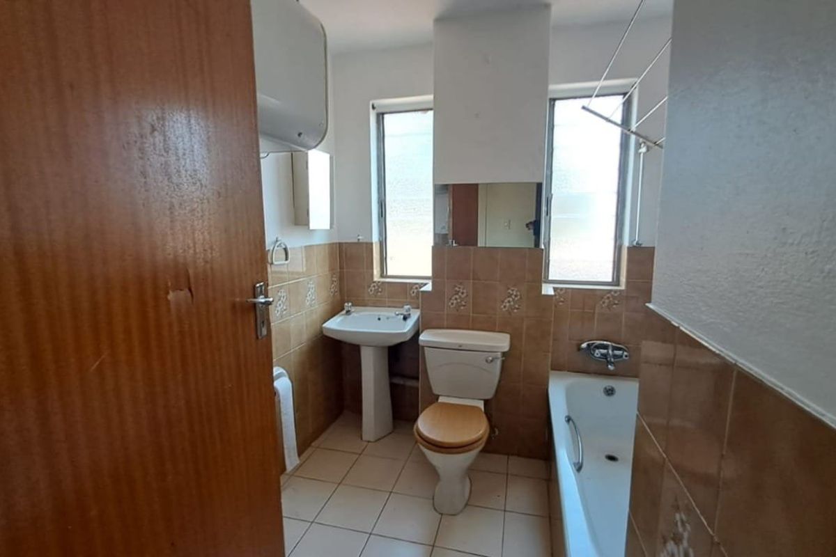 A functional bathroom featuring a pedestal basin, toilet, and bathtub with tiled finishes, requiring cosmetic updates to modernize the space.