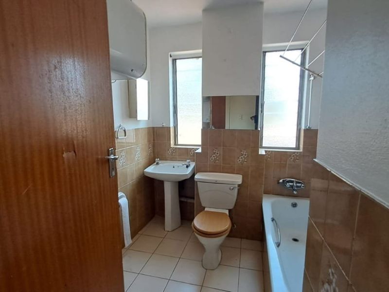 A functional bathroom featuring a pedestal basin, toilet, and bathtub with tiled finishes, requiring cosmetic updates to modernize the space.