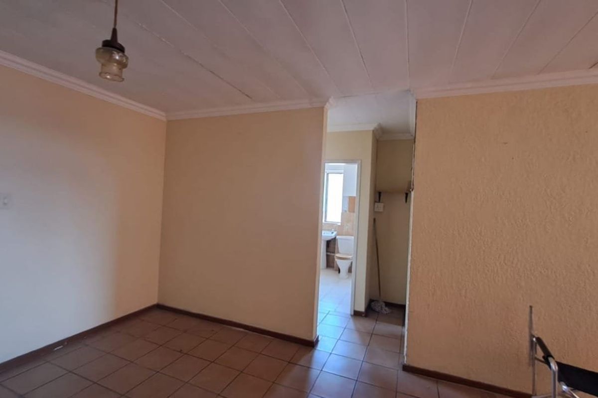 An empty living area featuring tiled flooring and coved ceilings, with a direct view into an adjacent bathroom.