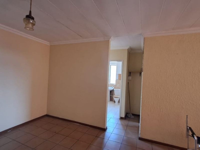 An empty living area featuring tiled flooring and coved ceilings, with a direct view into an adjacent bathroom.