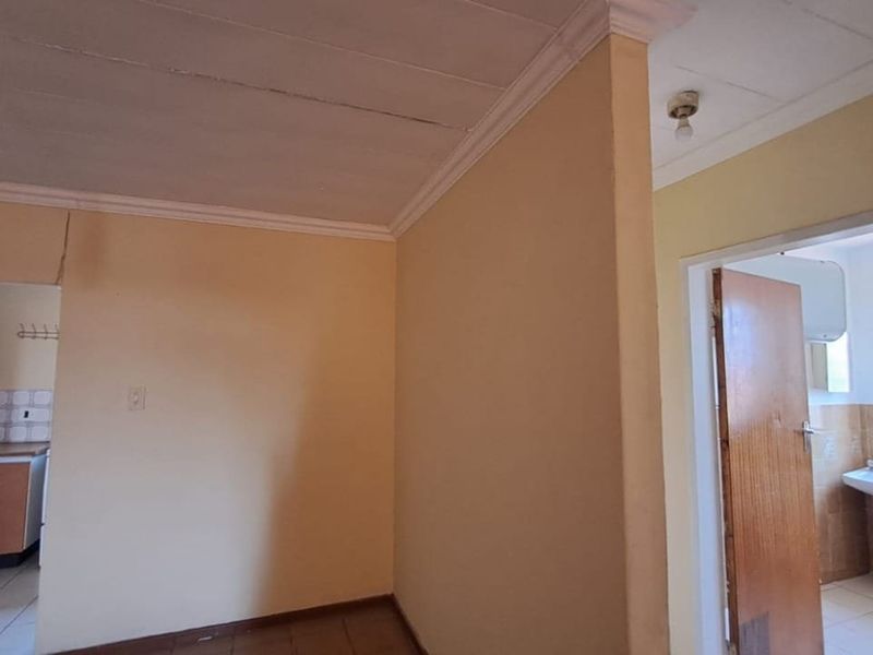 An open-plan living area featuring tiled floors and crown molding, with views into a dated kitchen and a bathroom with a pedestal sink.