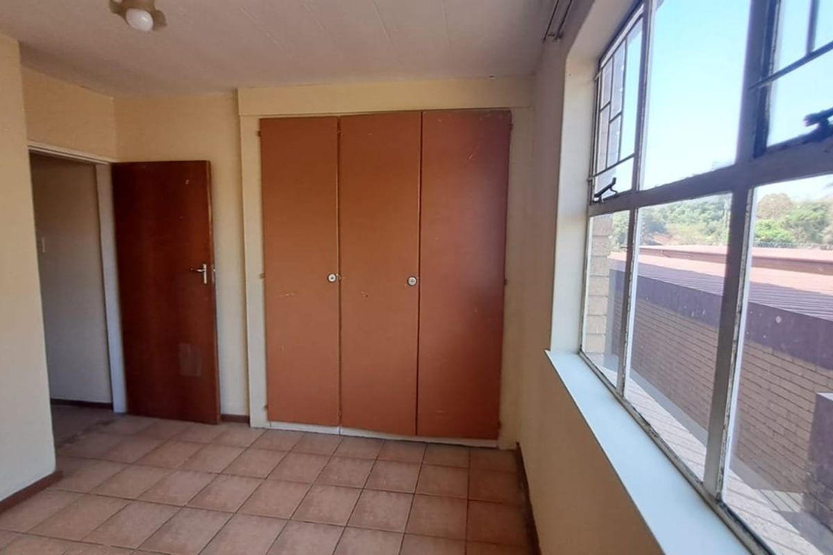 An empty bedroom featuring tiled flooring, built-in cupboards, and large steel-framed windows providing natural light.