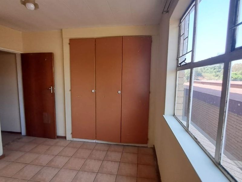 An empty bedroom featuring tiled flooring, built-in cupboards, and large steel-framed windows providing natural light.