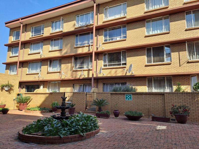 Rear view of a multi-story brick apartment building featuring a paved courtyard area with a central fountain and established perimeter wall.