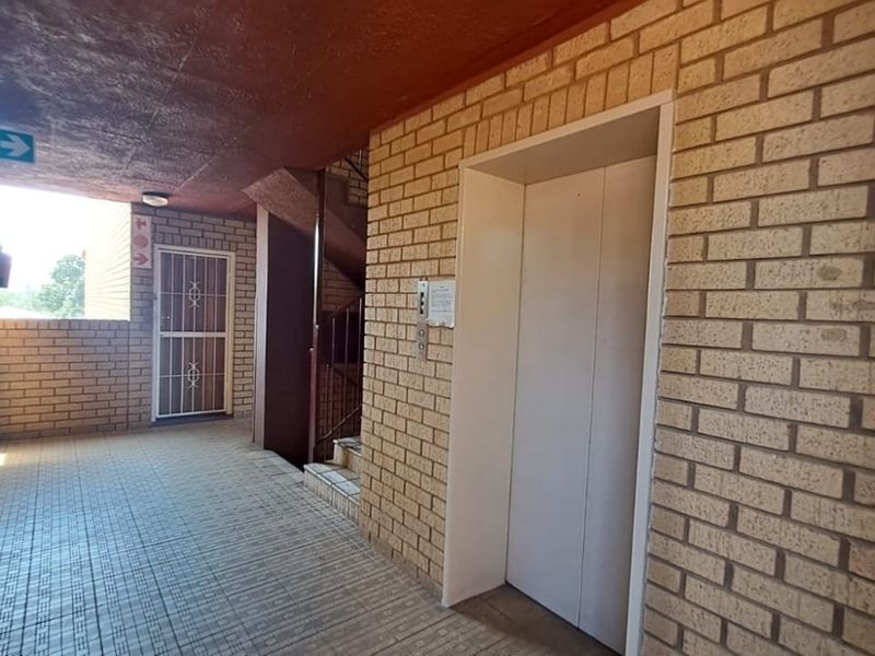 A communal apartment hallway featuring brick walls, tiled flooring, a functional elevator, and a secure metal gate leading to an entrance.