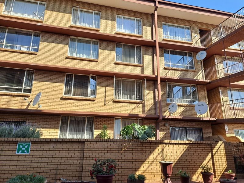 Rear elevation of a multi-story brick apartment building featuring multiple balconies, metal-framed windows with security bars, and various satellite dish installations.