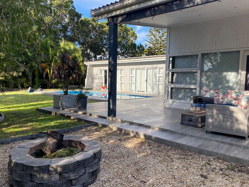 A spacious covered patio featuring tiled flooring, overlooking a private swimming pool and a stone fire pit in the garden area.