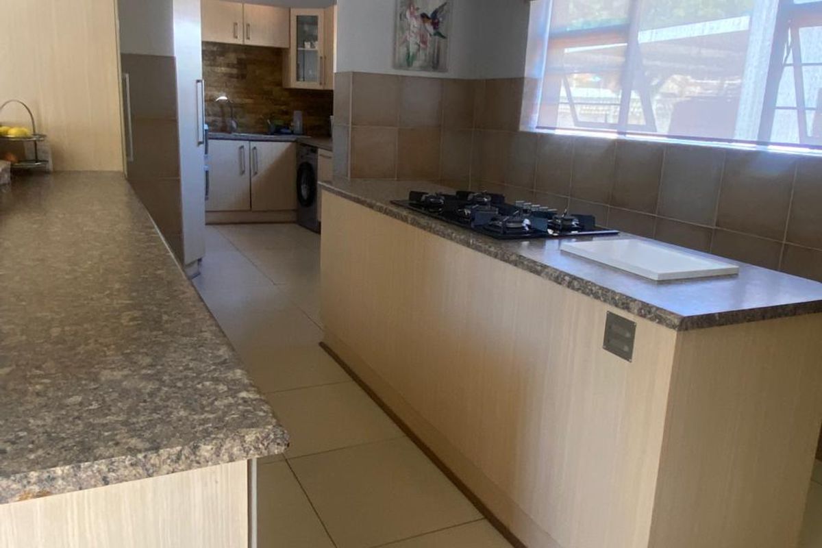 A functional kitchen featuring a central island with a gas cooktop, tiled backsplash, and an adjoining scullery area with additional cabinetry.