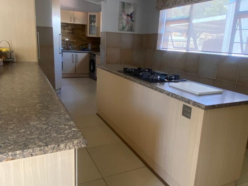 A functional kitchen featuring a central island with a gas cooktop, tiled backsplash, and an adjoining scullery area with additional cabinetry.