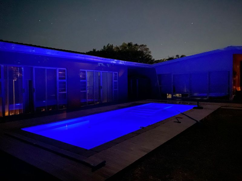 Night view of a rectangular swimming pool with blue underwater lighting, adjacent to the house with large sliding glass doors.
