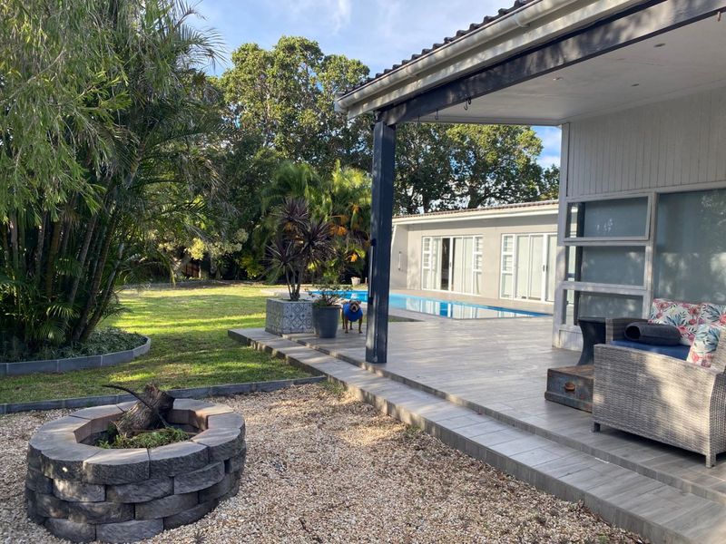 A spacious rear garden featuring a tiled patio, a built-in stone fire pit, and a swimming pool, perfect for outdoor entertaining.