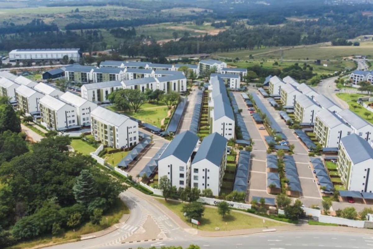 Aerial view of a modern residential apartment complex featuring multiple building blocks, paved parking areas, and landscaped communal grounds.