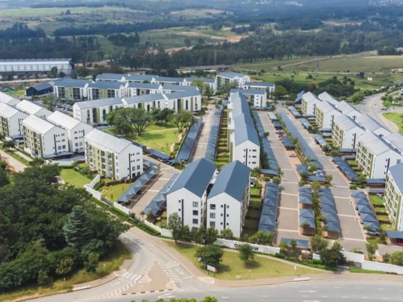 Aerial view of a modern residential apartment complex featuring multiple building blocks, paved parking areas, and landscaped communal grounds.